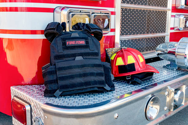 gilet balistique et casque rouge de pompier sur le pare-chocs de camion de feu. concept d’évolution du rôle de l’intervention des pompiers face aux fusillades de masse et au terrorisme - red vest photos et images de collection