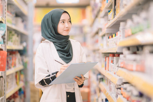 azjatycka nowoczesna muzułmańska farmaceutka z hidżabem rejestrująca poziom zapasów leku w aptece - counting instrument zdjęcia i obrazy z banku zdjęć