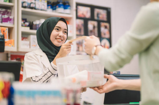 an asian muslim lady cashier take over the basket from her customer for check out payment an asian muslim lady cashier take over the basket from her customer for check out payment asian cashier stock pictures, royalty-free photos & images