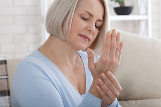 middle aged woman suffering from pain in hands. woman massaging her arthritic hand and wrist - osteoarthritis doctor medicine healthcare and medicine imagens e fotografias de stock