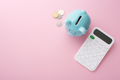 Piggy bank, calculator and coin on pink background, saving money concept, flat lay