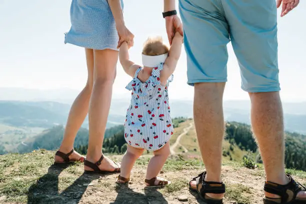 Photo of Mom, dad and daughter in the mountains enjoy and look at nature. View back down. Bottom view of legs. Young family spending time together on vacation, outdoors. The concept of family summer holiday.