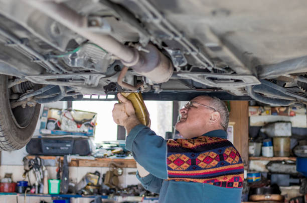 старший автомеханик проверяет и ремонтирует поднятую машину в своем гараже. - old men car oil стоковые фото и изображения