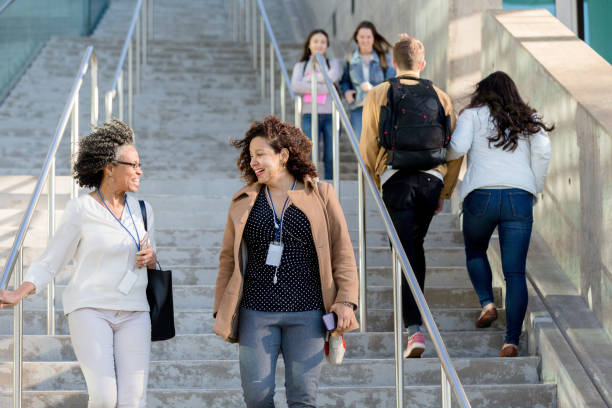 Female college professors walk together on campus Two female college professors talk with each other while descending an outdoor staircase on campus. community college stock pictures, royalty-free photos & images