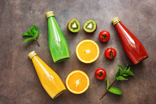 フラットは、暗い素朴な背景にボトル入りのジュースと果物や野菜の半分の様々な配置。ジュース、トマト、オレンジ、キウイの盛り合わせ。上から見る。 - kiwi vegetable cross section fruit ストックフォトと画像