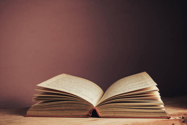 istock Open vintage ancient book. Pattern background for design. The book on a brown wooden table and red wall background. 1212214631