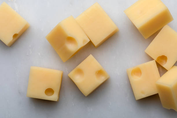 portions (cubes, dice) of emmental swiss cheese with scratcher. texture of holes and alveoli. on white marble background. - cheese emmental cheese swiss culture cutting board imagens e fotografias de stock