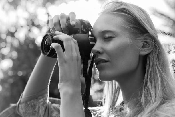 Professional woman photographer shooting photos outdoor. Art passion. A pretty blonde woman taking a photo outdoors. Vintage style black and white. Old fashion. black and white portrait photographers stock pictures, royalty-free photos & images
