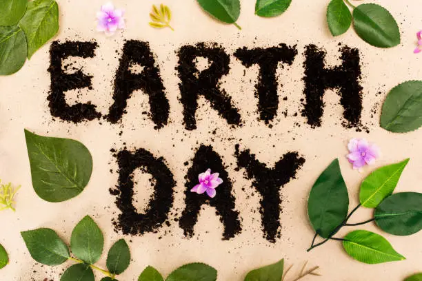 Photo of Top view of earth day lettering with leaves and buds on beige background