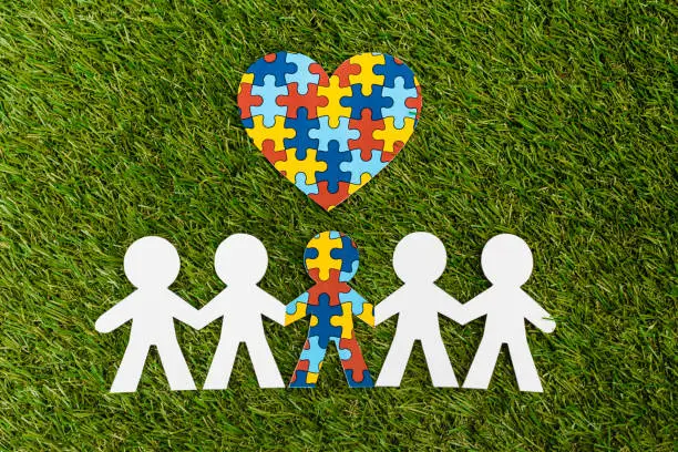 Top view of special kid with autism among another and decorative puzzle heart on green