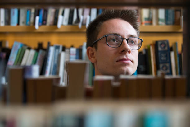istock Young Adult Man With Eyeglasses Between Bookshelfs 1212226670