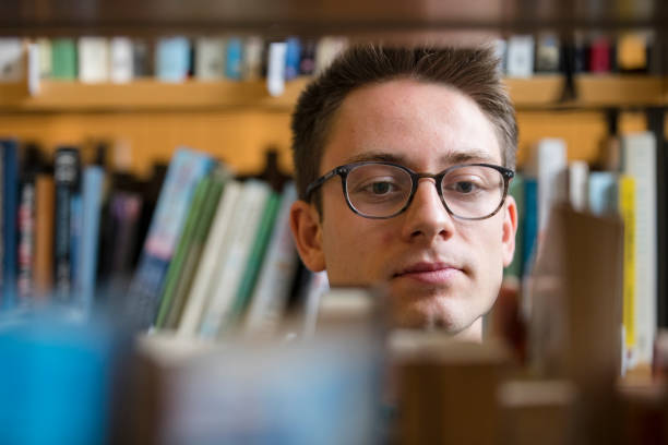 istock Student Picking Up a Book from Bookshelf in Library 1212226680
