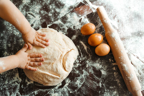 istock Kids hands, some flour, wheat dough and rolling-pin on the dark table. 1212229522