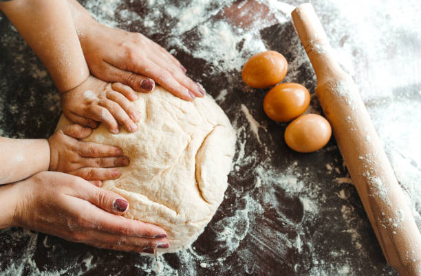 Hands of mother and son kneading a dough together. Photo. Hands of mother and son kneading a dough together. Mother and child hands prepares the dough with flour on dark wooden table. Bakery background. Cooking concept. baking bread stock pictures, royalty-free photos & images