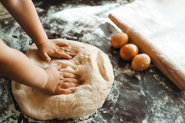 istock Kids hands, some flour, wheat dough and rolling-pin on the dark table. 1212229632