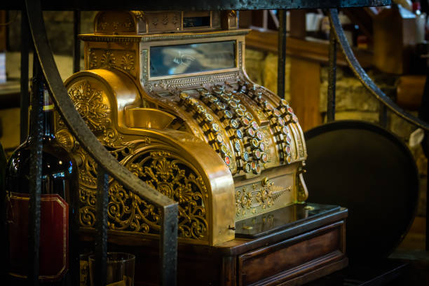 Brass antique and ornate cash register with selective focus. Glass and bottle of red wine in foreground and vintage moody background