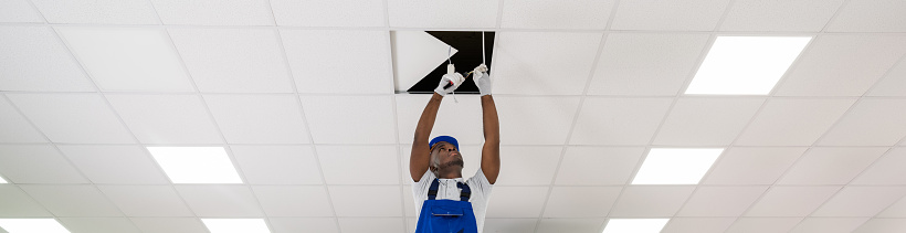 Young Male Electrician On Stepladder Installing Light On Ceiling