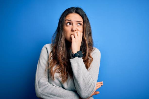 jeune belle femme brune utilisant le chandail occasionnel restant au-dessus du fond bleu regardant stressé et nerveux avec des mains sur la bouche mordant des ongles. problème d’anxiété. - bad habit fear emotional stress women photos et images de collection