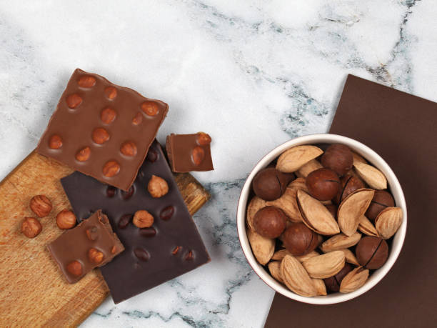 istock Broken chocolate bars, hazelnuts and raw inshell macadamia and almonds on gray marble background 1212239828