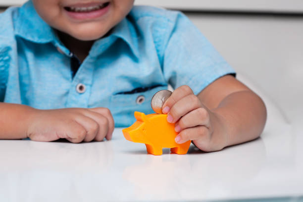 A young boy demonstrating fine motor skills by using a pincer grasp to hold a coin, before putting it into a small piggy bank slot. stock photo
