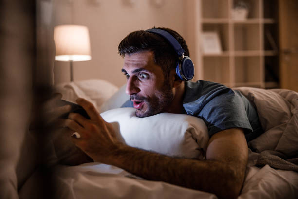 istock Funny guy with gadgets in bed stock photo 1212245196