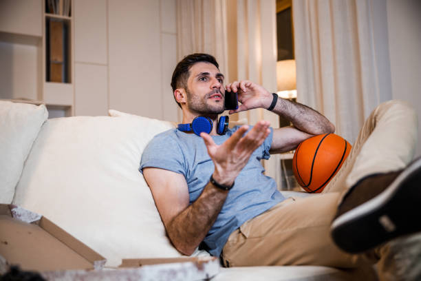 istock Young man speaking on phone on sofa stock photo 1212245239