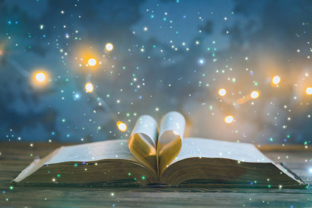 Old opened book, heart shaped paper sheets, dark background with stars toned vintage selective focus