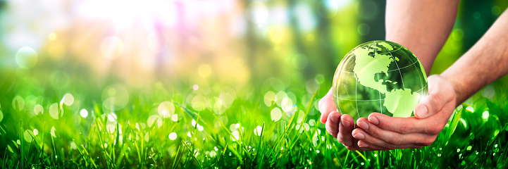 Hands Holding Crystal Earth In Lush Green Environment With Sunlight - Earth-Day Concept