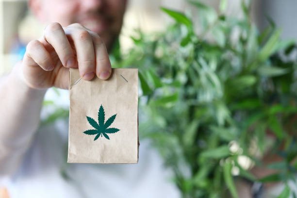 Male hand hold paper packet with marijuana symbol closeup background stock photo