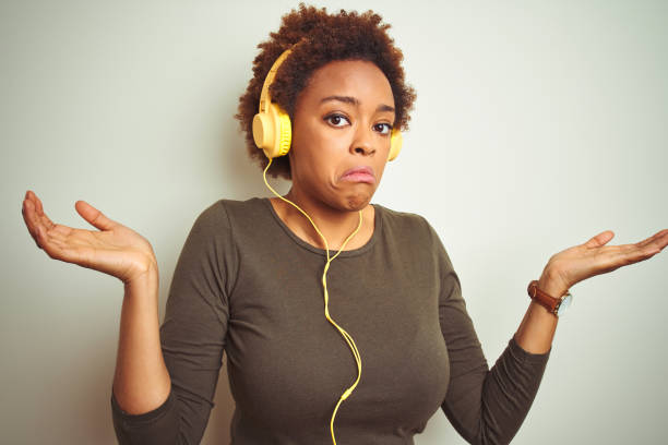 african american woman wearing headphones listening to music over isolated background clueless and confused expression with arms and hands raised. doubt concept. - head and shoulders audio imagens e fotografias de stock