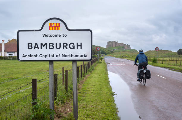 ciclista masculino indo em direção ao castelo de bamburgh, northumberland, inglaterra - bamburgh castle bamburgh road castle - fotografias e filmes do acervo