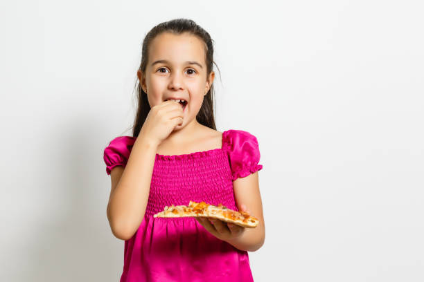 istock happy little girl eating pizza white background 1212249804