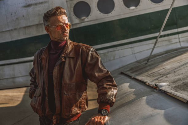 Waist up of handsome male in leather jacket looking away near plane stock photo