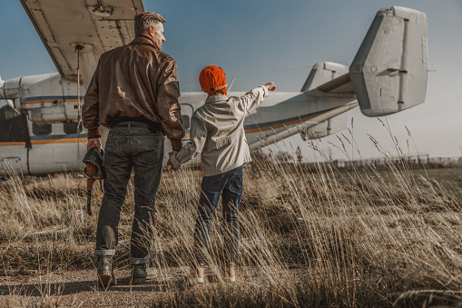 Little boy pointing to airplane while standing with his father outdoors stock photo