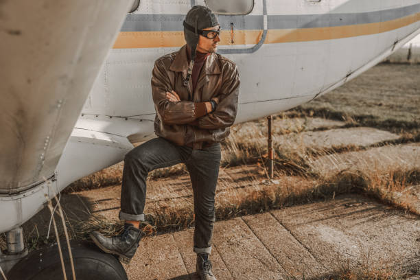 Full length of stylish pilot standing near airplane and looking away outdoors stock photo