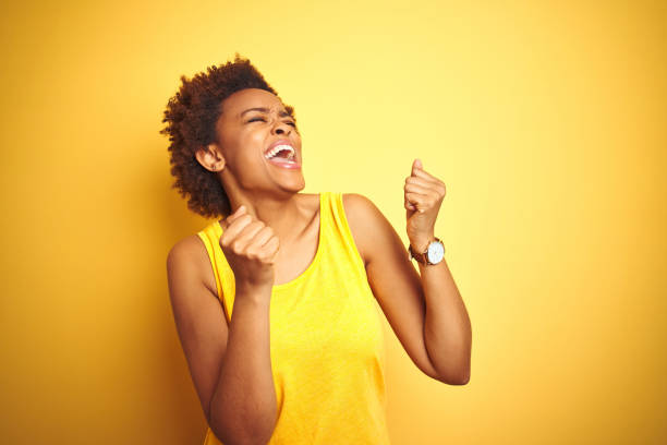 beauitul donna afroamericana che indossa maglietta estiva su sfondo giallo isolato molto felice ed emozionata facendo gesto vincitore con le braccia alzate, sorridendo e urlando per il successo. concetto di celebrazione. - estasi foto e immagini stock