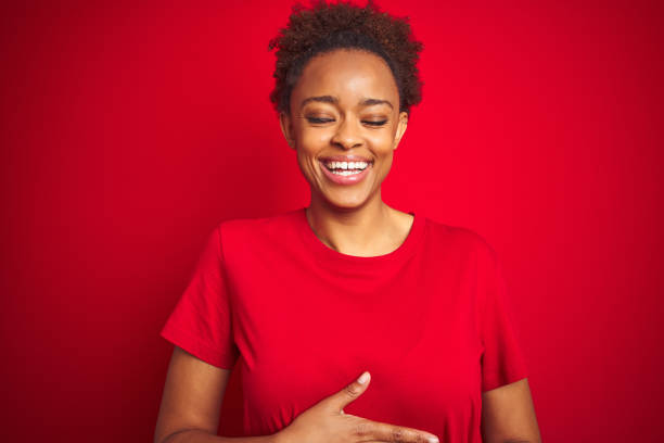 Young beautiful african american woman with afro hair over isolated red background smiling and laughing hard out loud because funny crazy joke with hands on body. Young beautiful african american woman with afro hair over isolated red background smiling and laughing hard out loud because funny crazy joke with hands on body. people laughing hard stock pictures, royalty-free photos & images