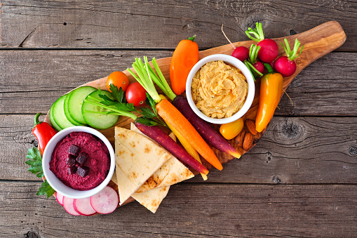 Assortment of fresh vegetables and hummus dip on a serving board. Top view on a rustic wood background.