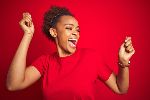 Young beautiful african american woman with afro hair over isolated red background Dancing happy and cheerful, smiling moving casual and confident listening to music
