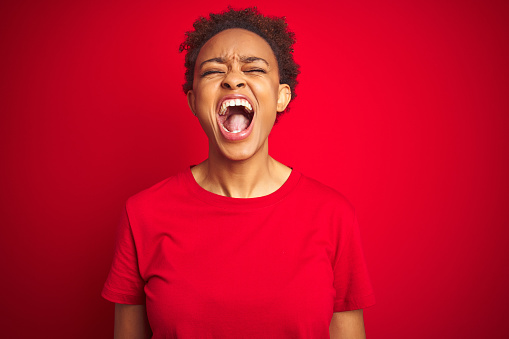 Joven hermosa mujer afroamericana con pelo afro sobre el fondo rojo aislado enojado y loco gritando frustrado y furioso, gritando de ira. Ira y concepto agresivo. photo