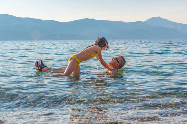 Father and Daughter Playing with Waves and Laughing on Summer Beach