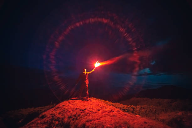 Photo of The man with a red firework stick standing on a mountain. evening night time