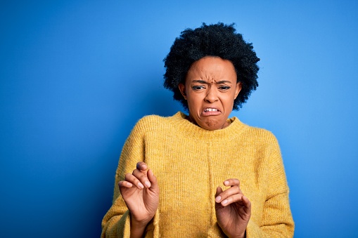 Young beautiful African American afro woman with curly hair wearing yellow casual sweater disgusted expression, displeased and fearful doing disgust face because aversion reaction.