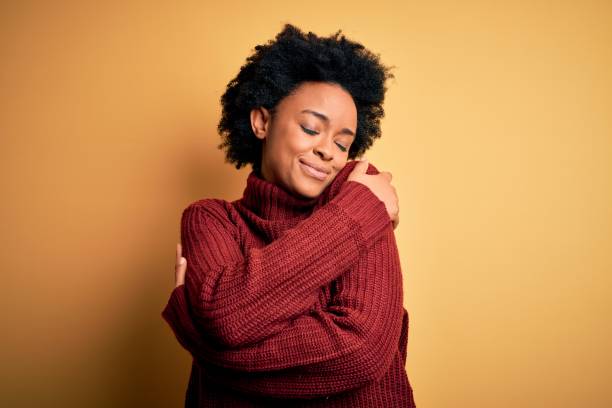 young beautiful african american afro woman with curly hair wearing casual turtleneck sweater hugging oneself happy and positive, smiling confident. self love and self care - self love imagens e fotografias de stock