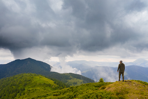 The man standing on the mountain against rainy clouds