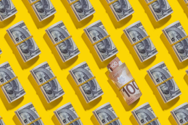 istock Canadian dollar and American dollar rolls on yellow background 1212263538