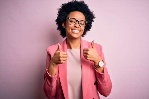 Young beautiful African American afro businesswoman with curly hair wearing pink jacket success sign doing positive gesture with hand, thumbs up smiling and happy. Cheerful expression and winner gesture. Young beautiful African American afro businesswoman with curly hair wearing pink jacket success sign doing positive gesture with hand, thumbs up smiling and happy. Cheerful expression and winner gesture. thumbs up stock pictures, royalty-free photos & images