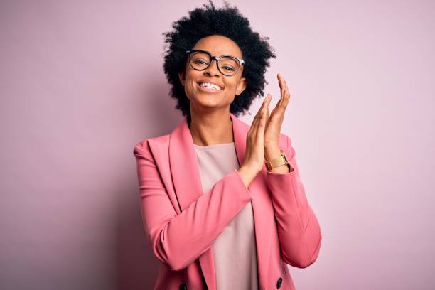 joven hermosa afroamericana afro mujer de negocios con el pelo rizado usando chaqueta rosa aplaudiendo y aplaudiendo felices y alegres, sonriendo manos orgullosas juntos - ovacionar fotografías e imágenes de stock