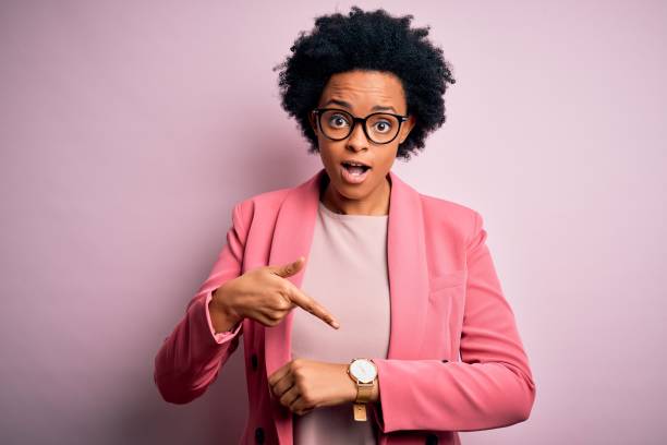 junge schöne afroamerikanische afro geschäftsfrau mit lockigen haaren trägt rosa jacke in eile zeigen, um zeit zu beobachten, ungeduld, verärgert und wütend für fristverzögerung - impatient stock-fotos und bilder