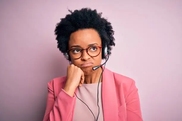 Photo of Young African American call center operator woman with curly hair using headset thinking looking tired and bored with depression problems with crossed arms.